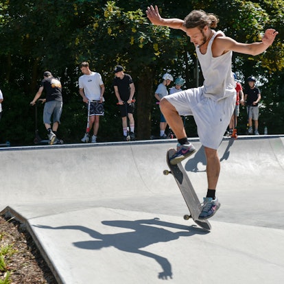 Zu sehen ist ein junger Mann, der einen Trick mit seinem Skateboard versucht.