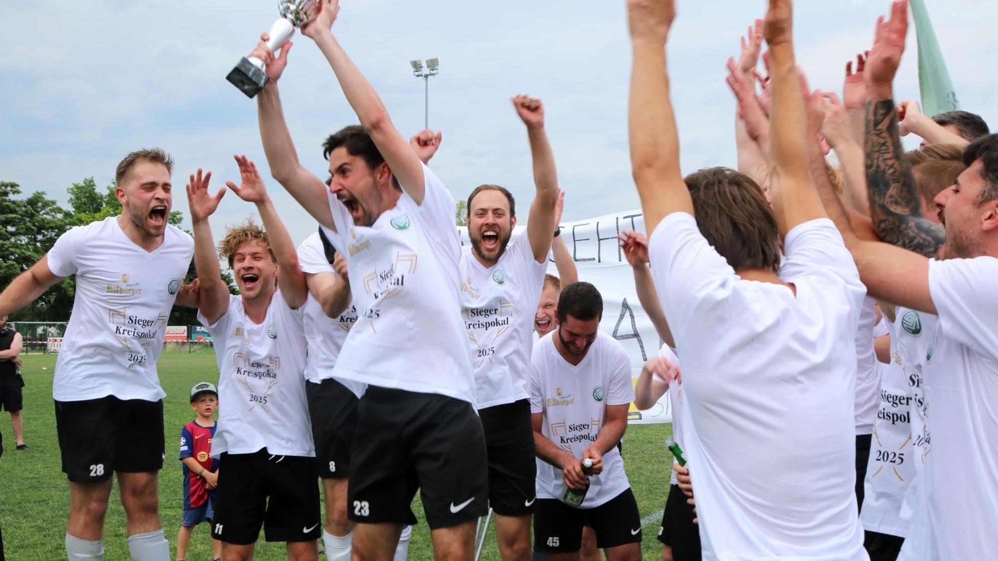 FlaKi-Kapitän Lukas Mager reckt den Pokal in die Höhe. Er und seine Mitspieler jubeln.