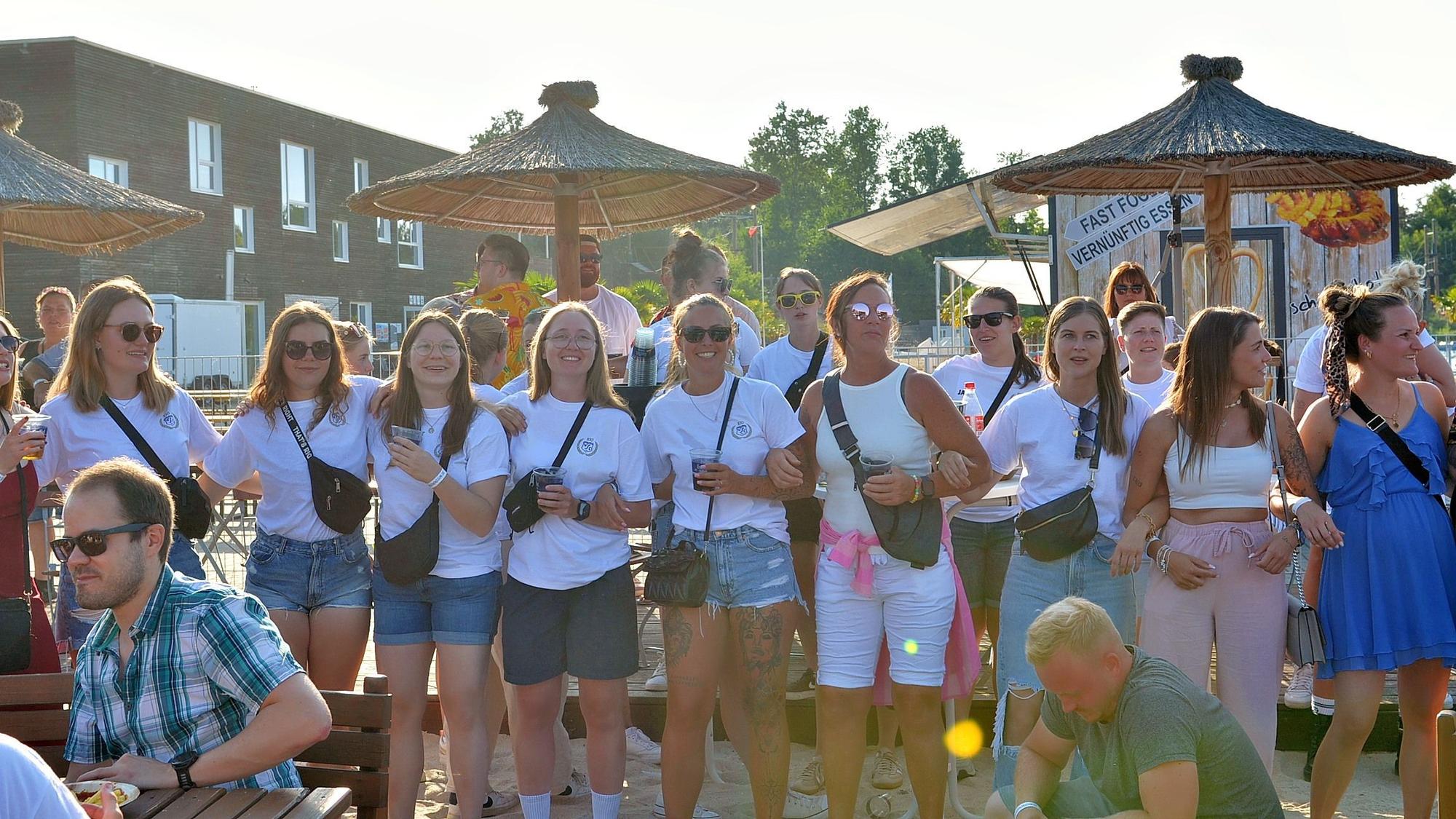 Das Bild zeigt zwei Reihen von jungen Frauen, die sich untergehakt haben. Die meisten tragen weiße T-Shirts.