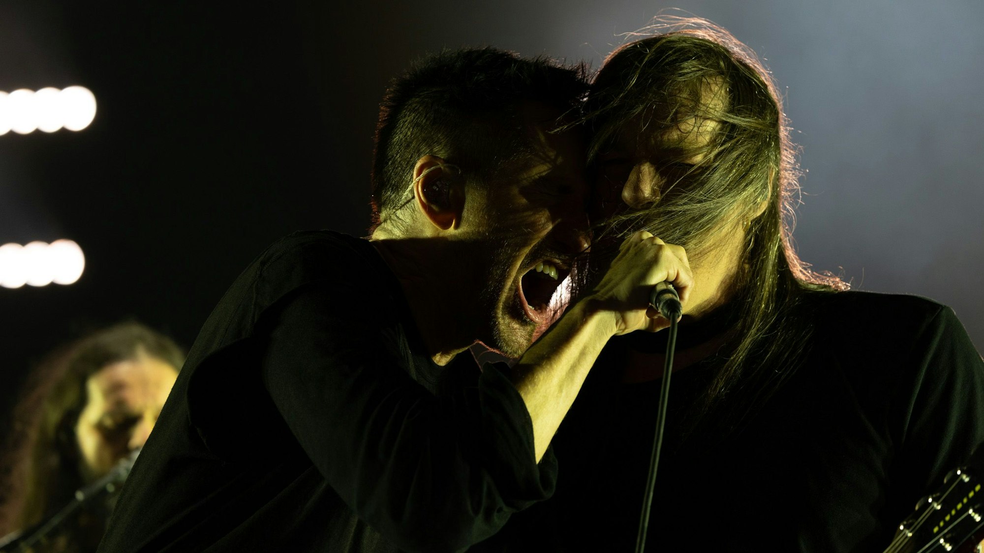Trent Reznor lehnt sich an einen langhaarigen Mitmusiker, brüllt ins Mikrofon.