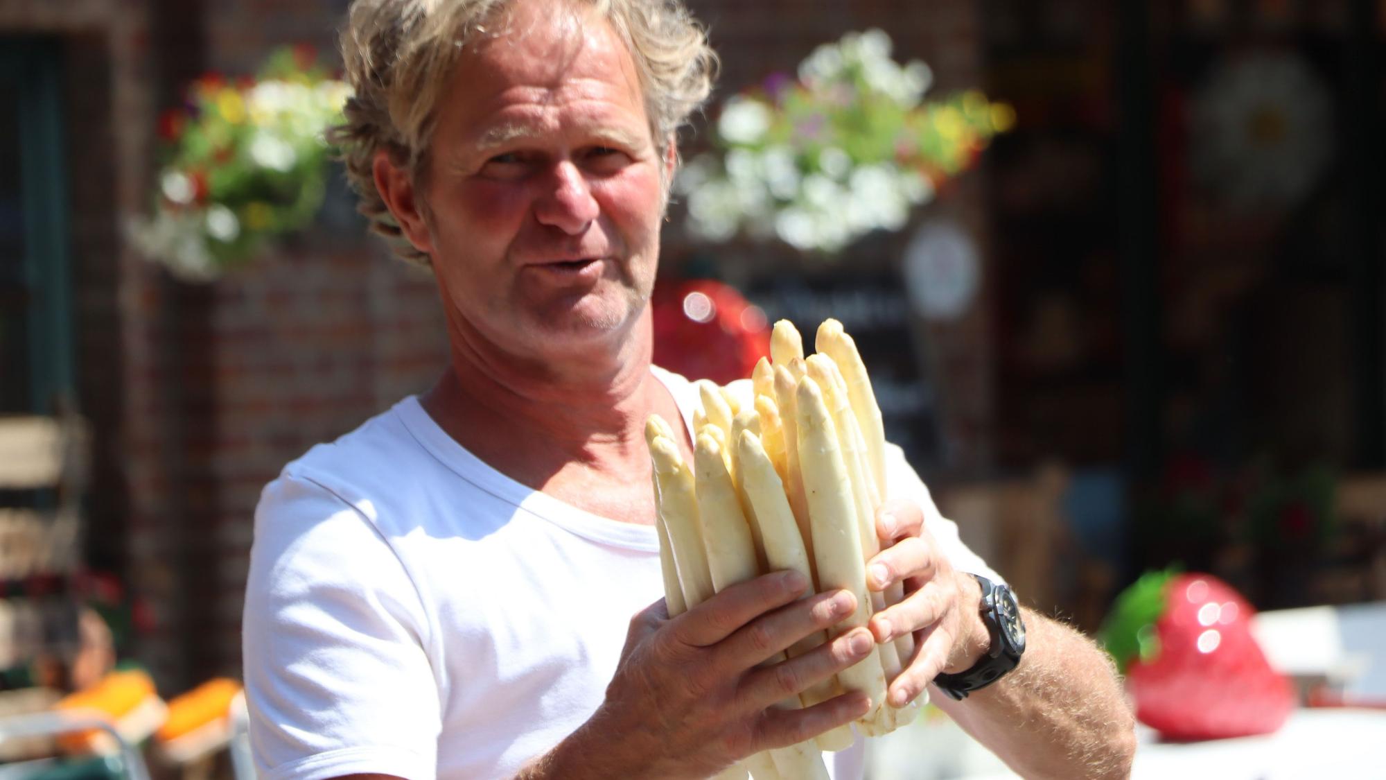 Auf dem Bild ist ein Landwirt zu sehen, der Spargel in den Händen hält.