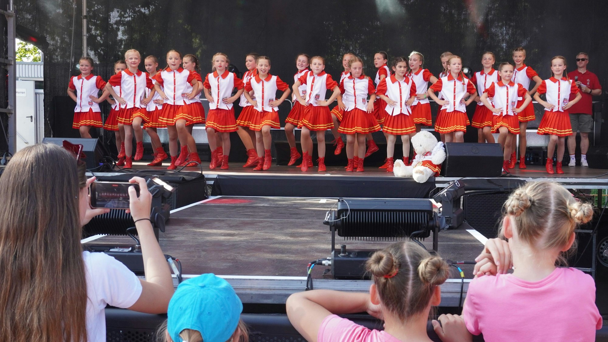 Auf dem Bild ist eine Kindertanzgruppe auf einer Bühne zu sehen.