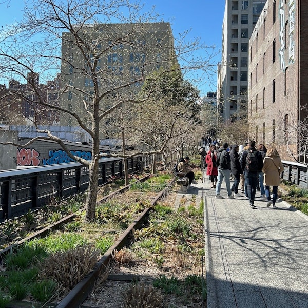 Auf einem von einem Geländer eingefassten Fußweg mit Begrünung sind Menschen unterwegs.