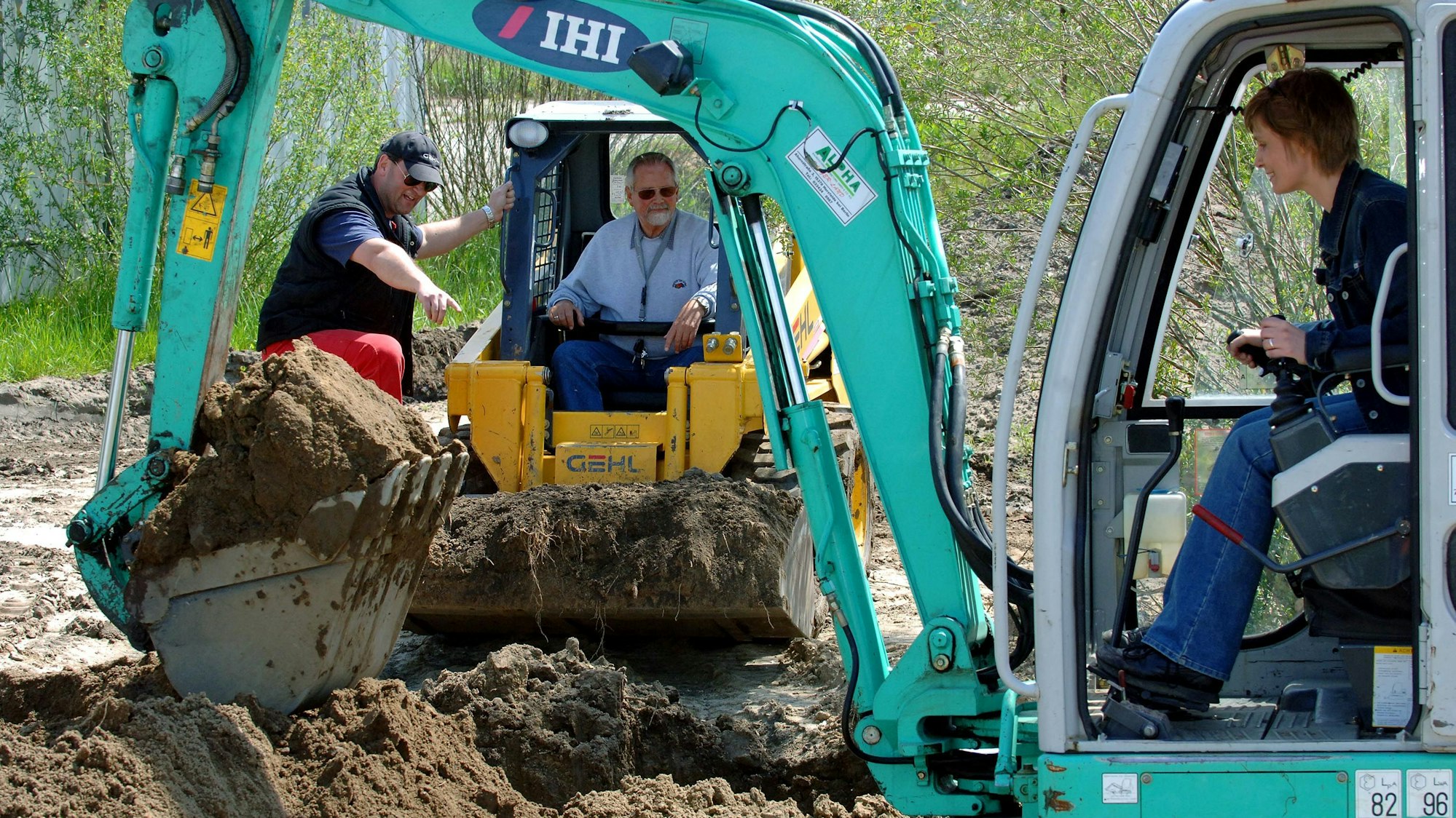 Ein Mann und eine Frau bedienen zwei Minibagger in einer Erdgrube.