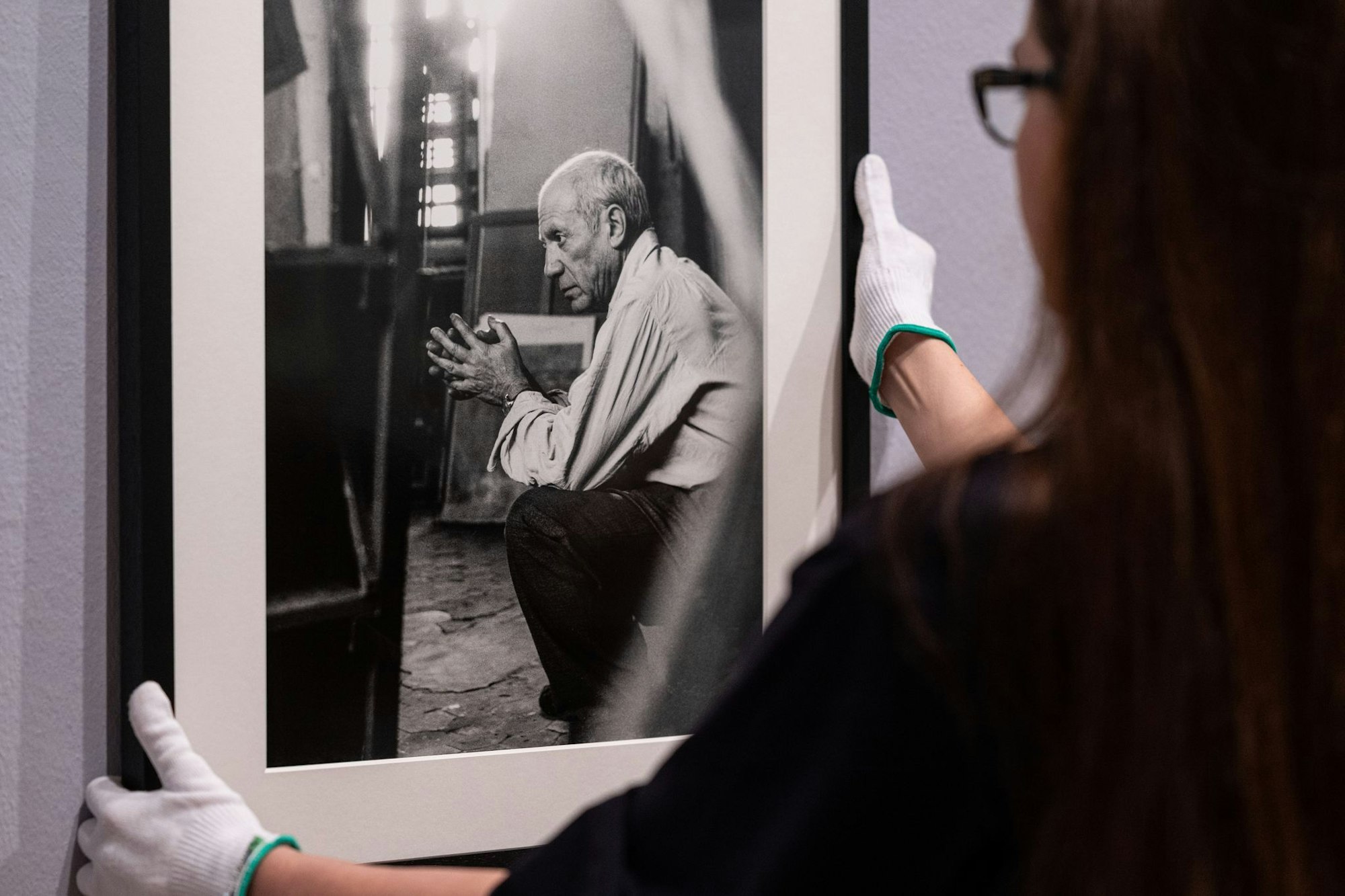 Eine Mitarbeiterin hängt ein eingerahmtes Foto von Pablo Picasso des Fotografen Herbert List an die Wand.