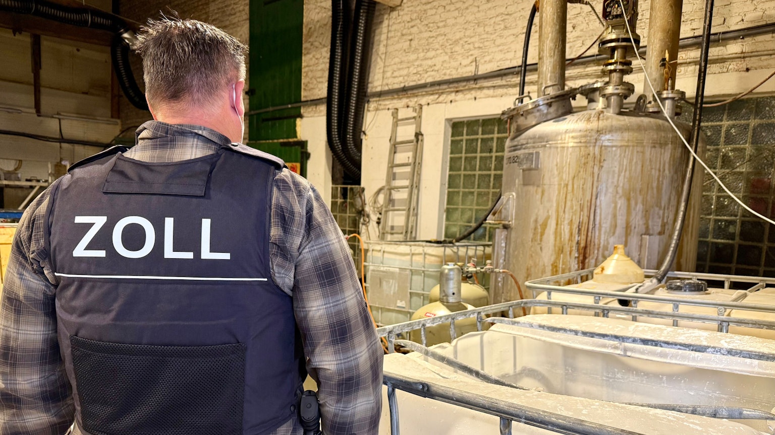 Das Bild zeigt einen Zollbeamten auf einer Hofanlage in Kerpen, wo illegal Drogen hergestellt wurden.