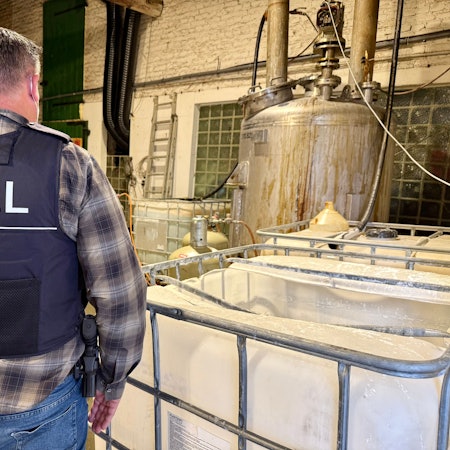 Das Bild zeigt einen Zollbeamten auf einer Hofanlage in Kerpen, wo illegal Drogen hergestellt wurden.
