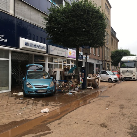Das Bild zeigt eine von Schlamm überzogene Fahrbahn, Sperrmüll sowie Autos und einen Lastwagen, die von den Fluten mitgerissen wurden.