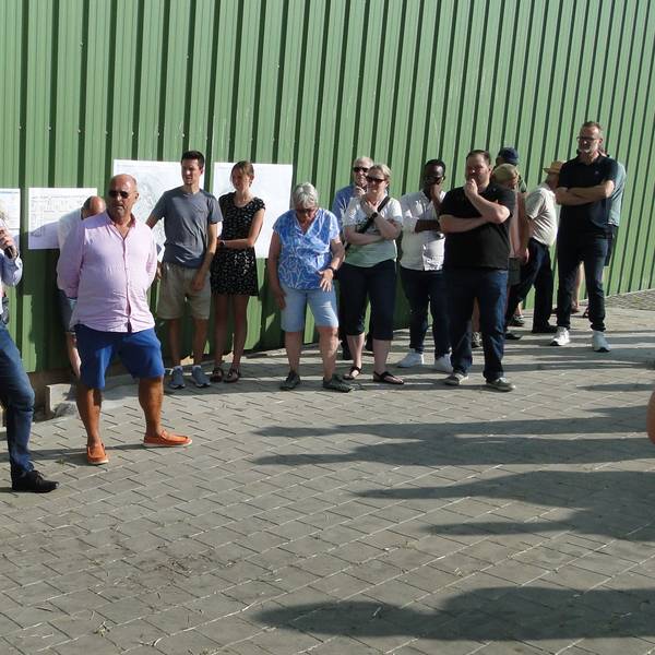 Mehrere Menschen stehen im Halbkreis vor einer großen Halle mit grüner Wand.
