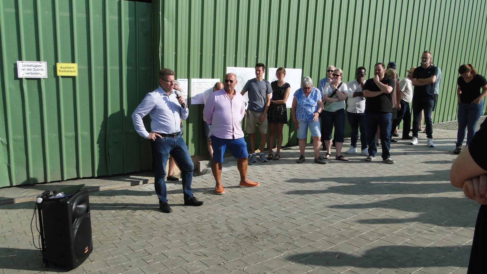 Mehrere Menschen stehen im Halbkreis vor einer großen Halle mit grüner Wand.