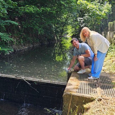 Thomas Scholzen kniet neben dem Wehr, Sabine Preiser-Marian steht daneben.