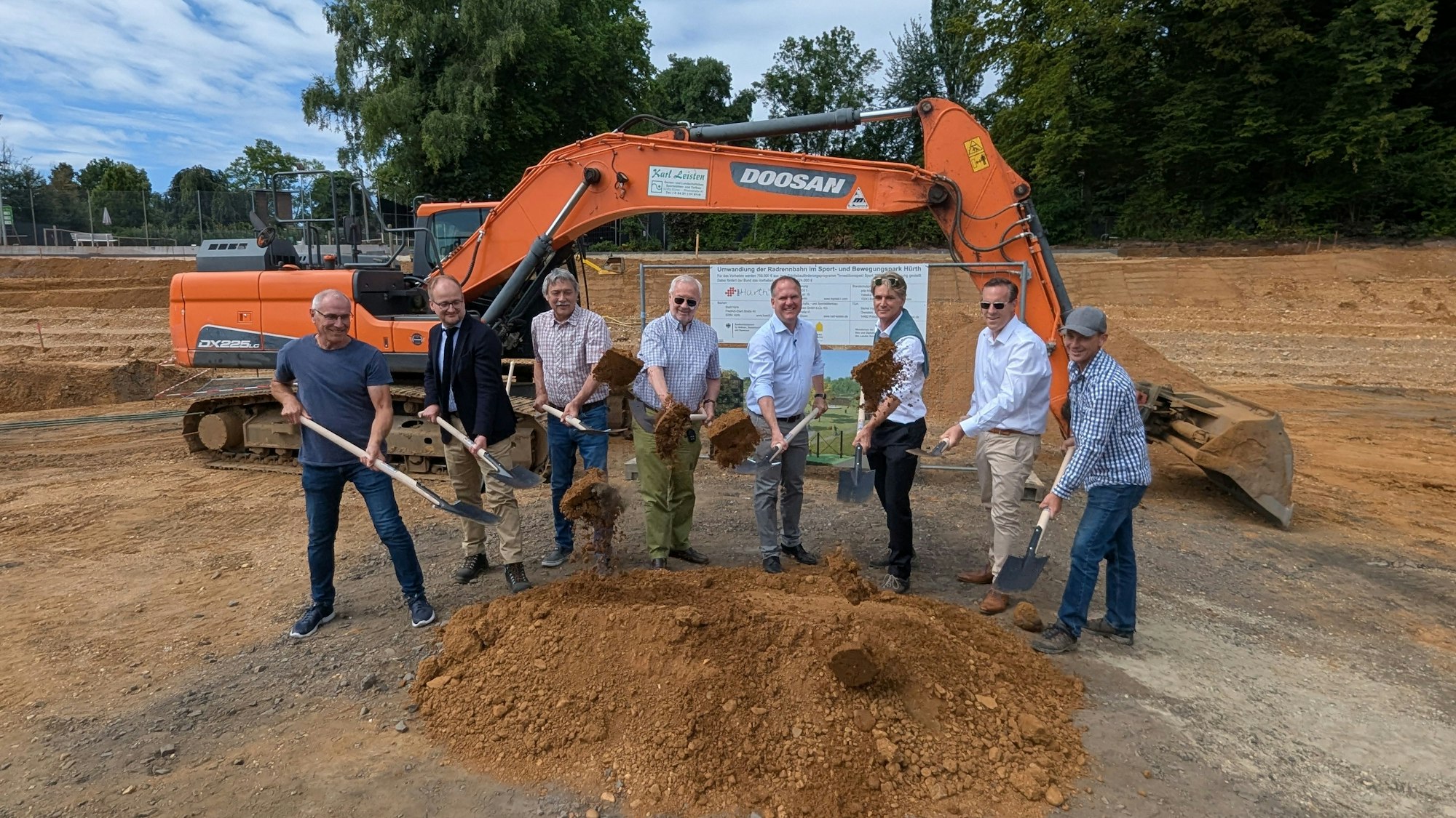 Das Foto zeigt eine Gruppe von Männern beim symbolischen Spatenstich auf der Baustelle in der ehemaligen Radrennbahn.