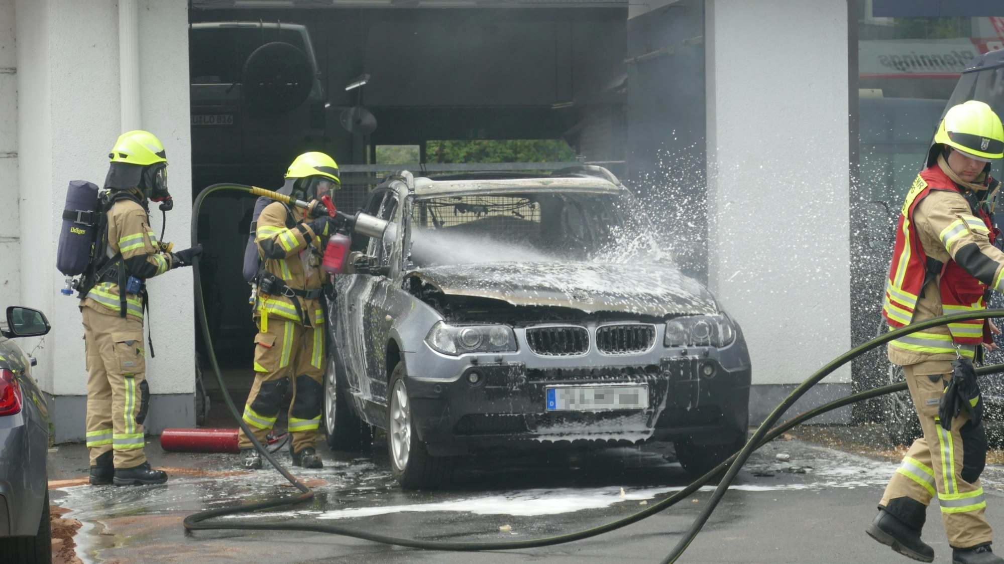 Feuerwehrleute besprühen ein Auto, das in Vollbrand stand, mit Schaum, um alle Glutnester zu ersticken.