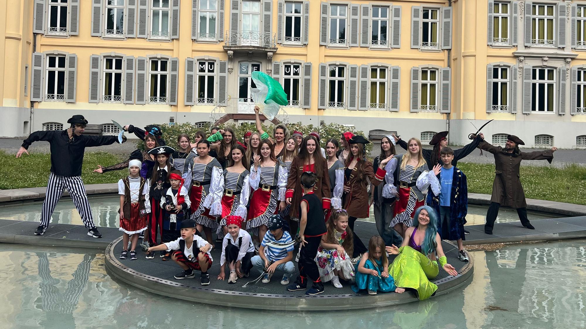 Kostümierte Tänzerinnen und Tänzer stehen vor einem Schloss.