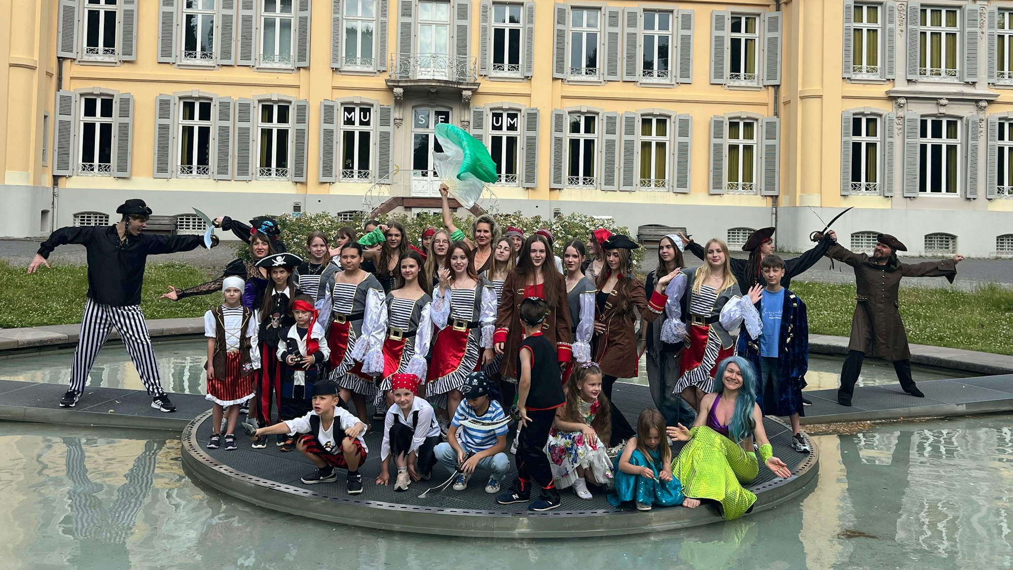 Kostümierte Tänzerinnen und Tänzer stehen vor einem Schloss.