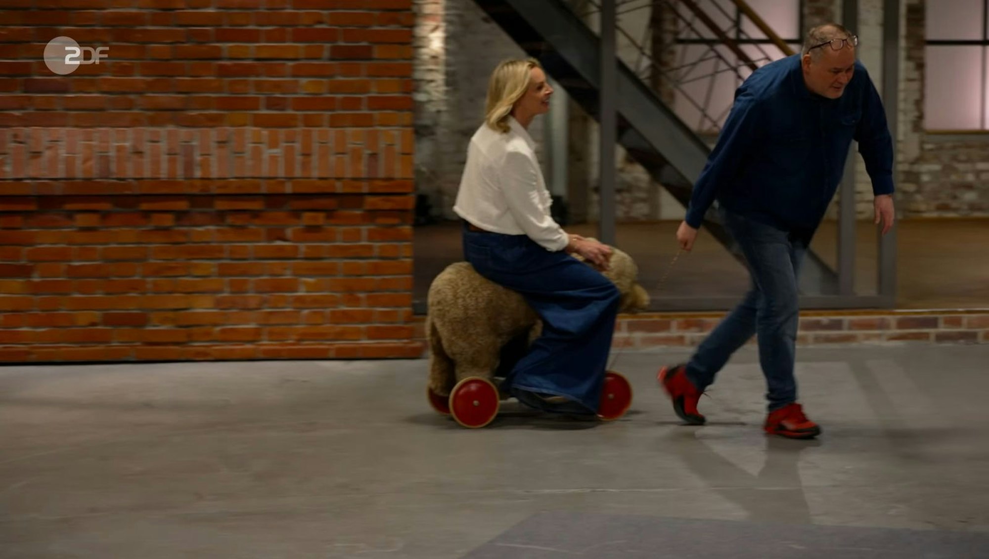 Dass der Steiff-Koloss bei den Händlern für Aufregung sorgen würde, war absehbar. Walter „Waldi“ Lehnertz rief galant: „Junge Frau, nehmen Sie Platz“, und Susanne Steiger sattelte den Bären. Ab ging die wilde Fahrt! (Bild: ZDF)