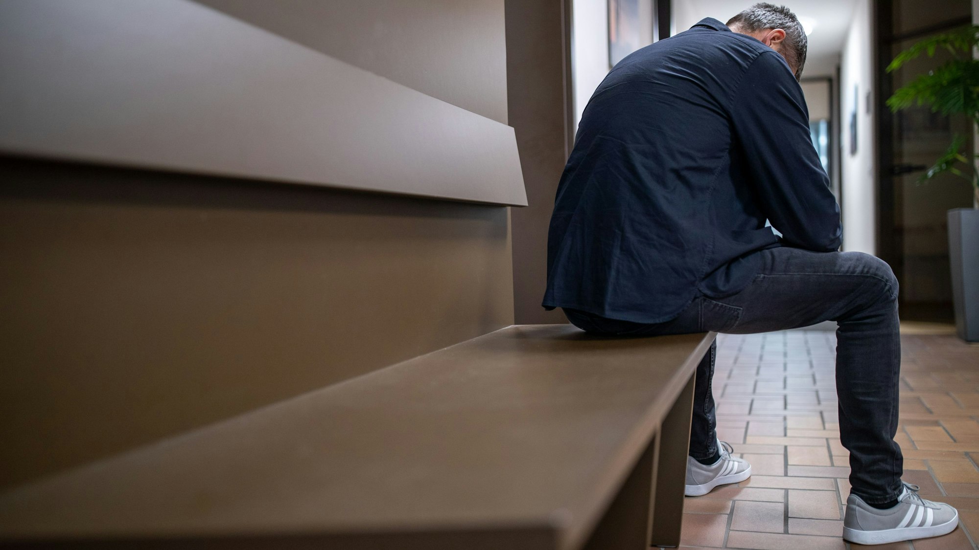 Ein Mann sitzt mit gesenktem Kopf auf einer Bank.