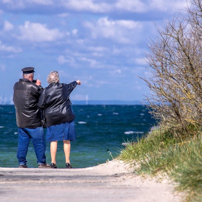 Ein Rentnerpaar steht am ansonsten menschenleeren Strand und schaut aufs Meer. (Archivbild)