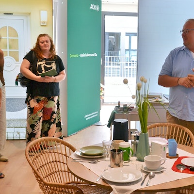 In der Mitte steht ein gedeckter Tisch, dahinter Sebastian Schmitz.