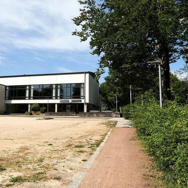 Im Vordergrund ist ein geschotterter Parkplatz, im Hintergrind die Grenzlandhalle in Hellenthal.
