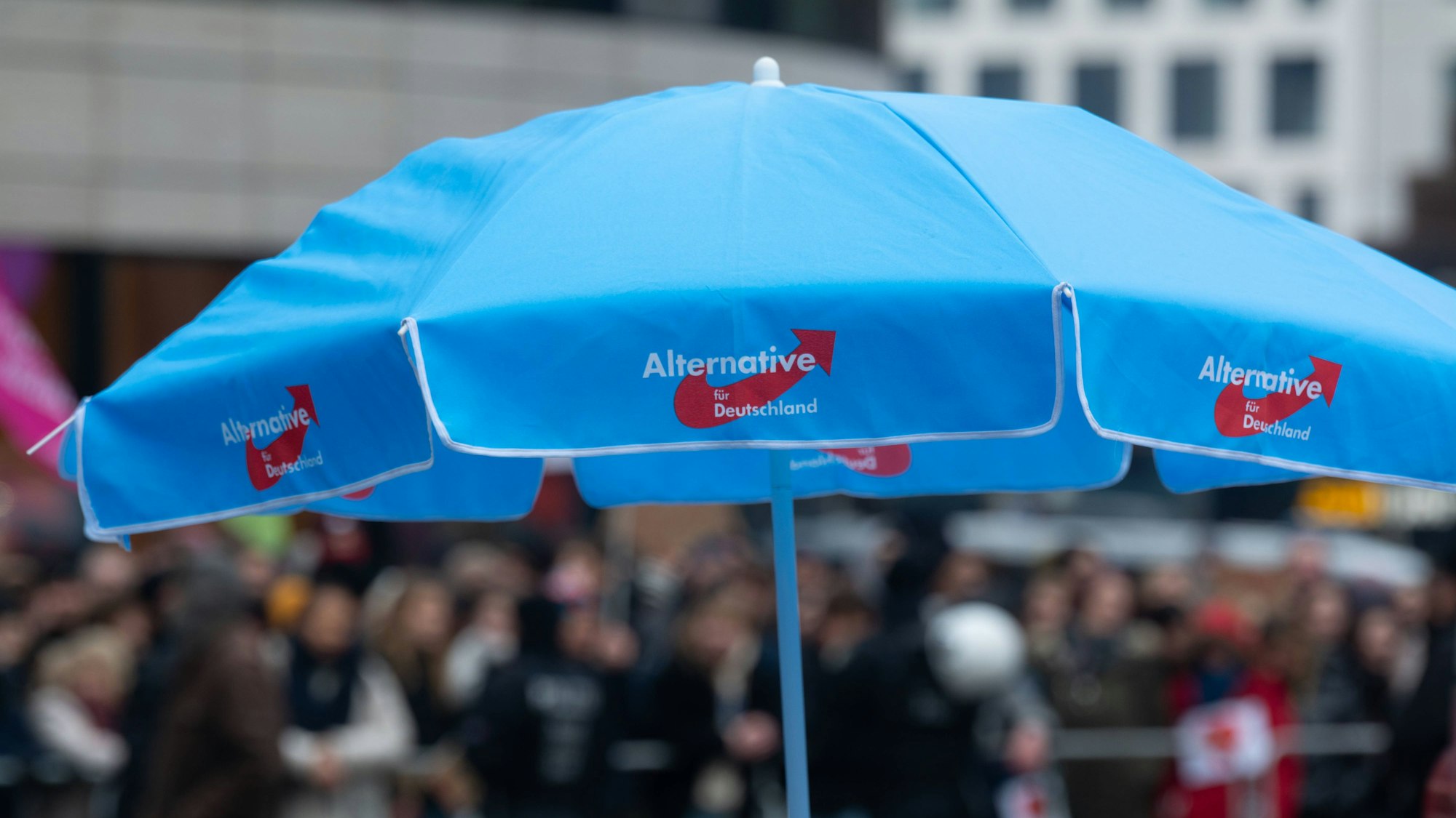 Ein blauer AfD-Sonnenschirm steht bei einer Veranstaltung auf einem Platz.
