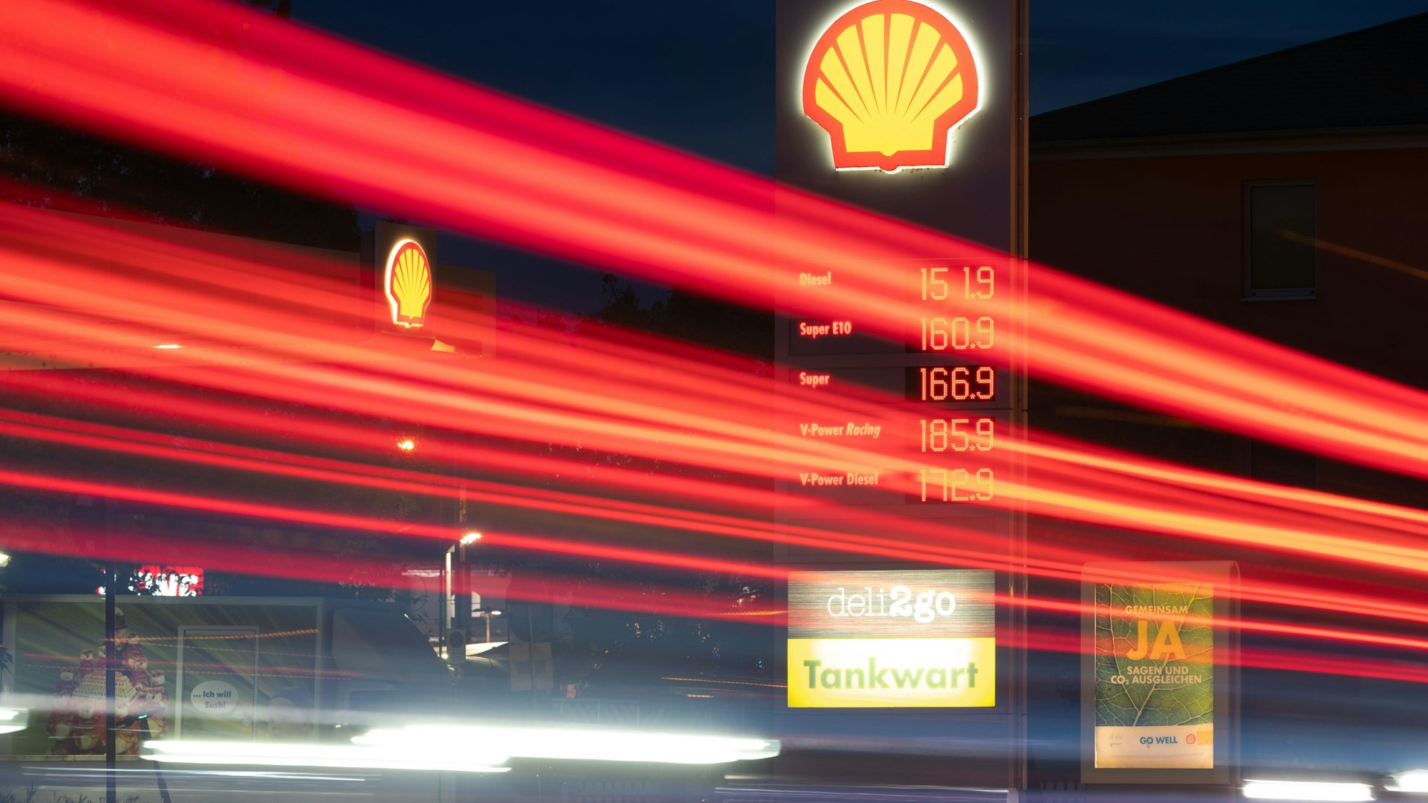 20.10.2021, Sachsen, Dresden: Die Scheinwerfer vorbeifahrender Fahrzeuge ziehen auf einer Straße Lichtspuren während im Hintergrund die Preistafel einer Tankstelle die Benzinpreise anzeigt. Foto: Sebastian Kahnert/dpa-Zentralbild/dpa +++ dpa-Bildfunk +++