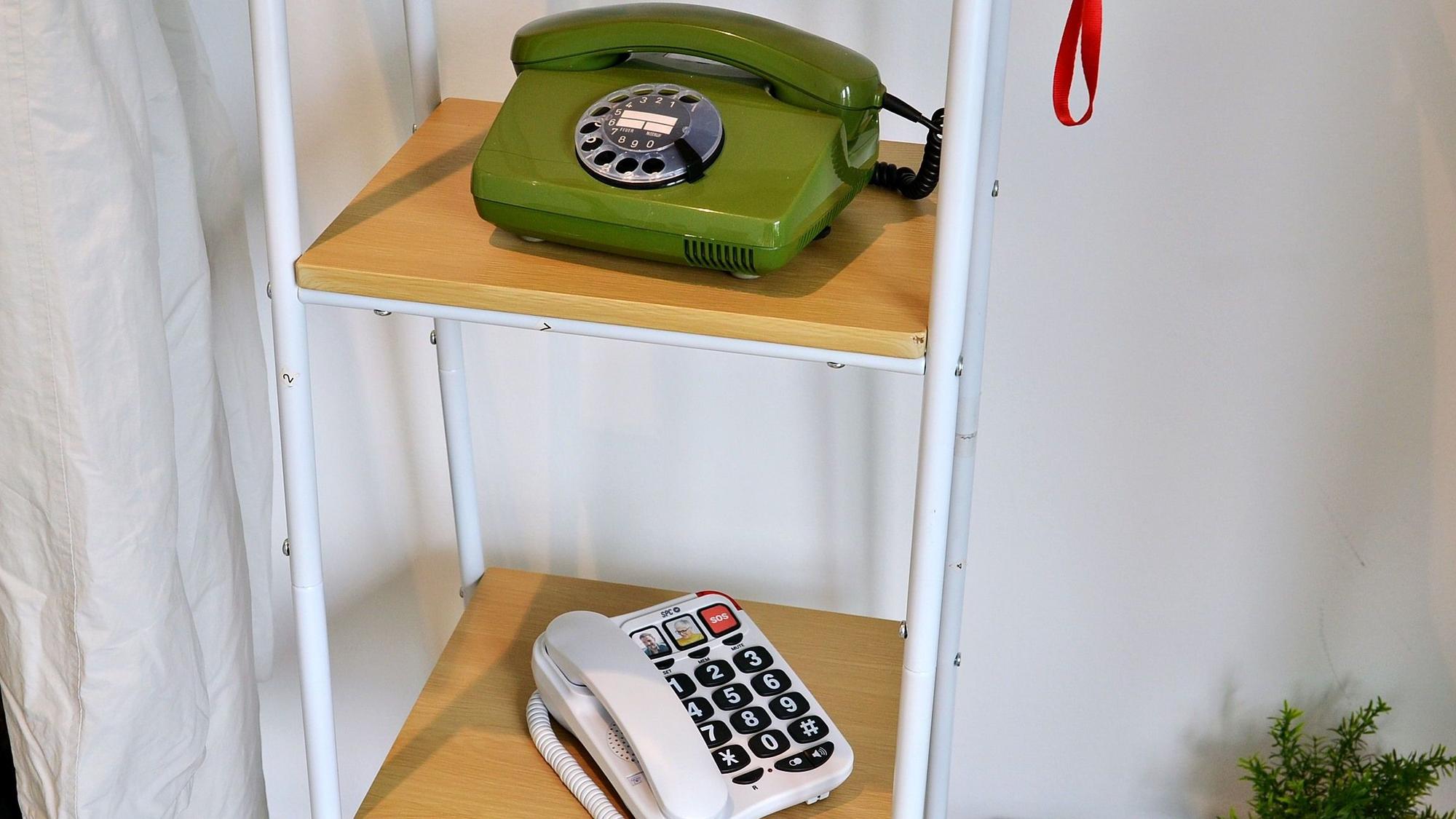 In einem Regal stehen ein altes Wählscheibentelefon und ein Telefon mit großen Tasten.