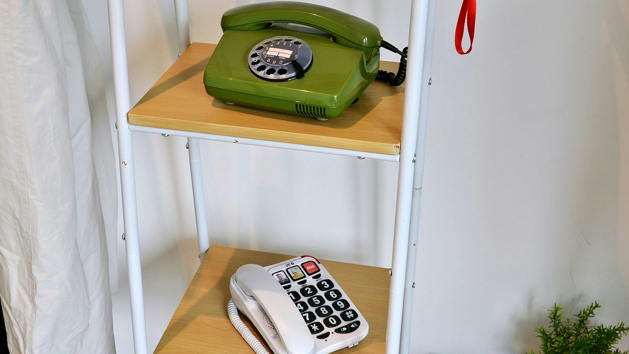 In einem Regal stehen ein altes Wählscheibentelefon und ein Telefon mit großen Tasten.