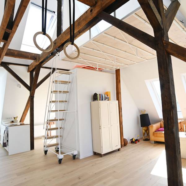 Zu sehen ist das mit Möbeln (Schrank, Sofa, Sessel, Kommoden) eingerichtete Loft T in Sülz. Eine Treppe führt nach oben.