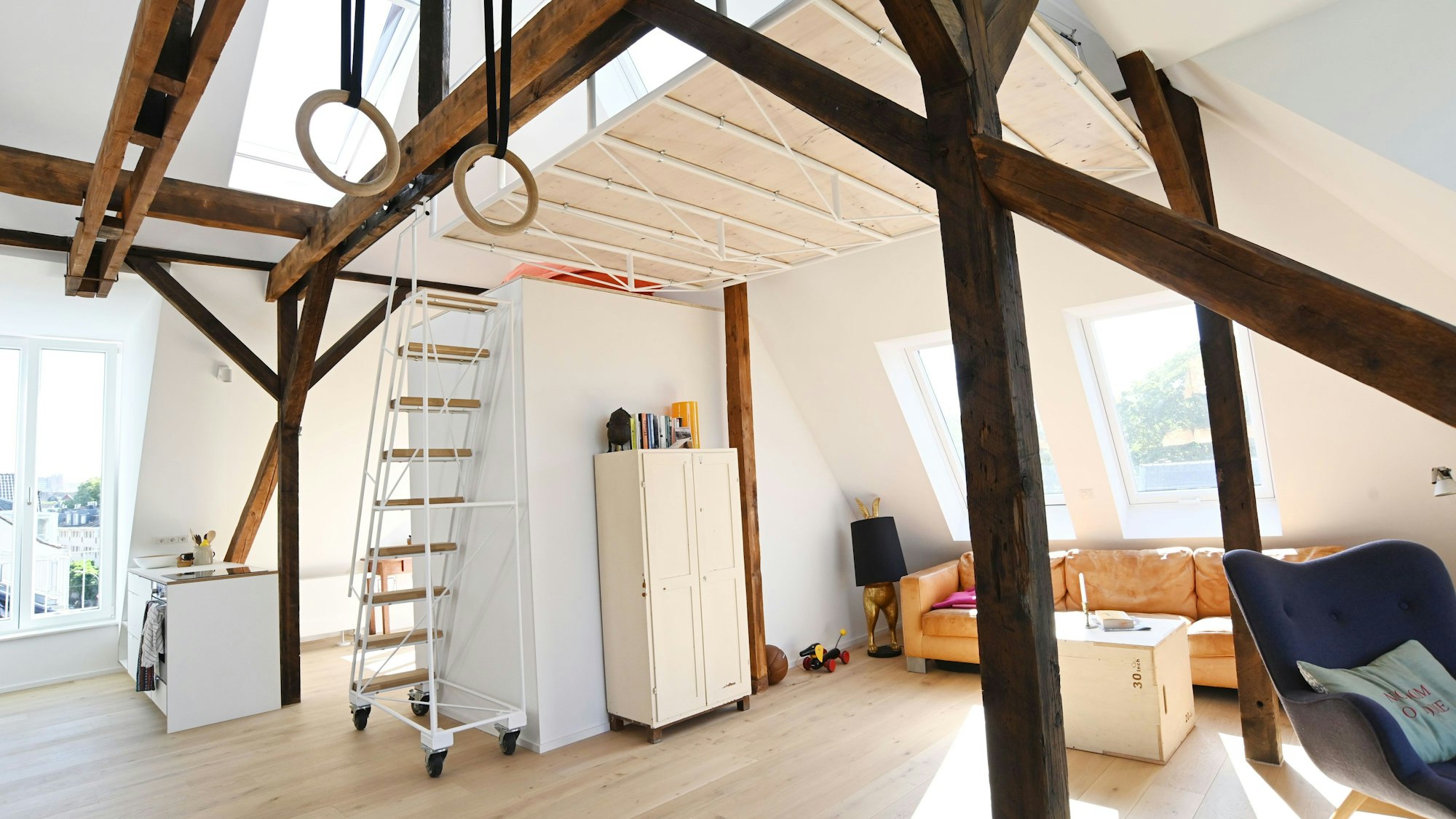 Zu sehen ist das mit Möbeln (Schrank, Sofa, Sessel, Kommoden) eingerichtete Loft T in Sülz. Eine Treppe führt nach oben.