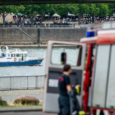 Ein Polizeiboot auf dem Rhein und ein Einsatzwagen der Feuerwehr am Ufer (Symbolfoto).