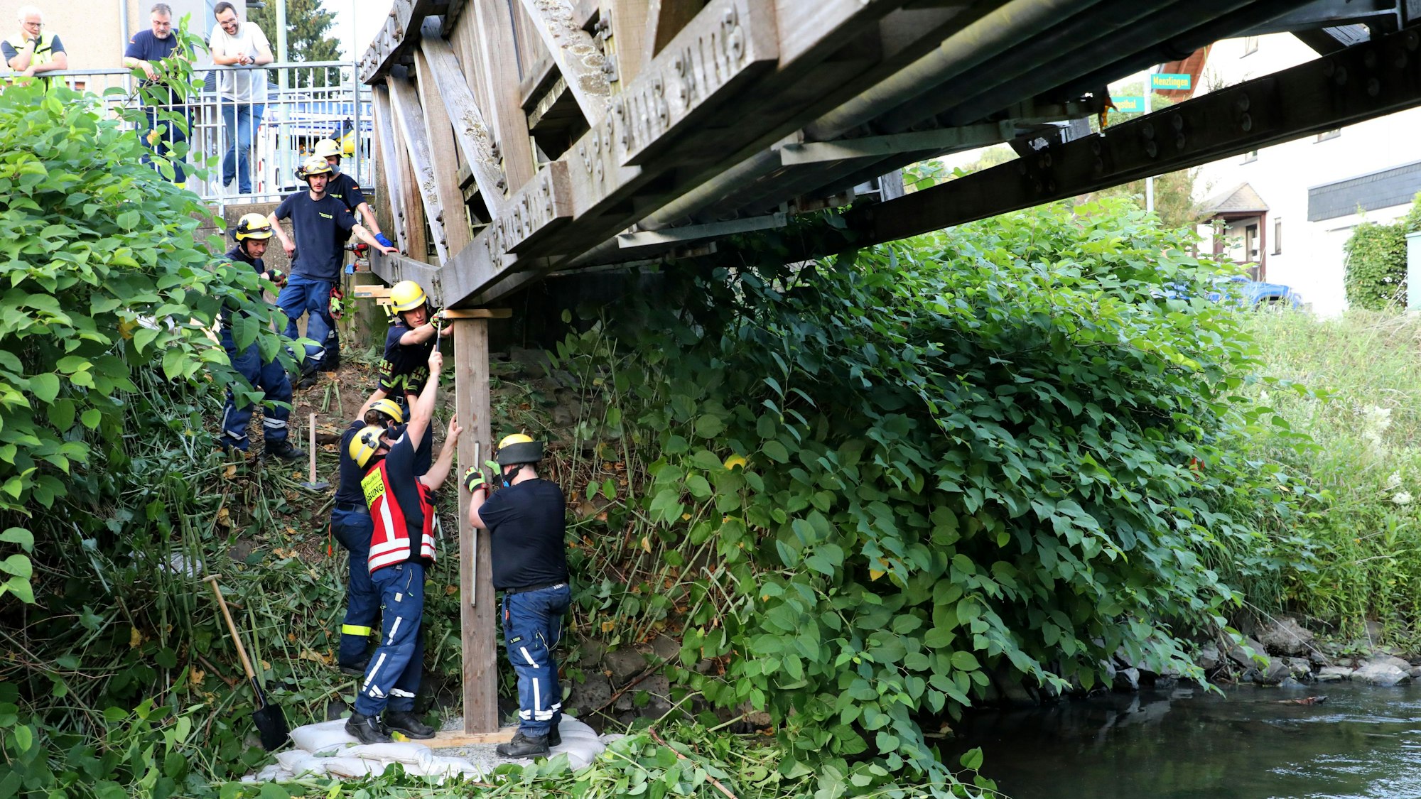 THW-Helfer stehen auf einer angeschütteten Insel im Fluss und montieren eine Holzstütze.
