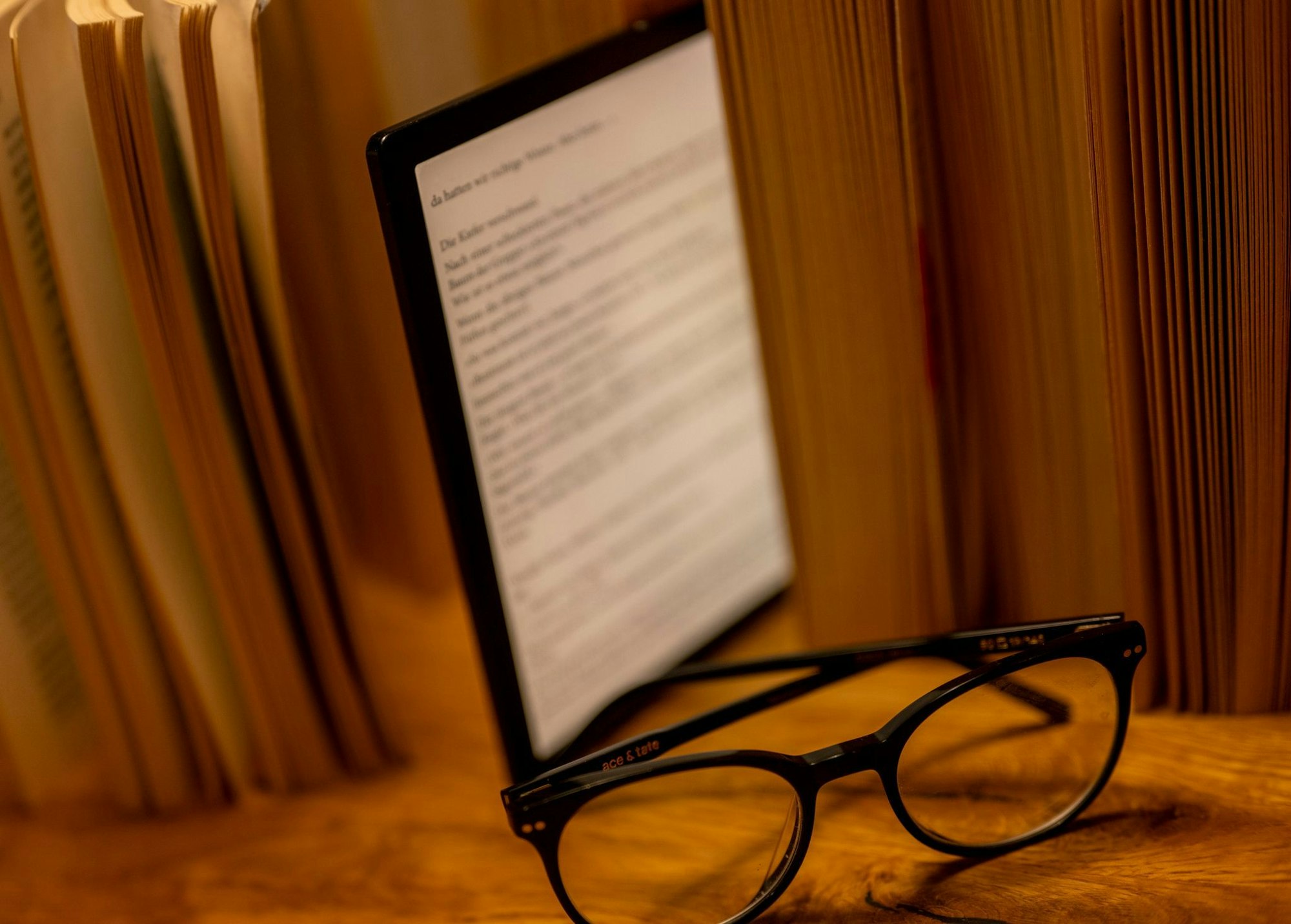 Ein E-Book steht zwischen einer Reihe Bücher, davor liegt eine Brille.