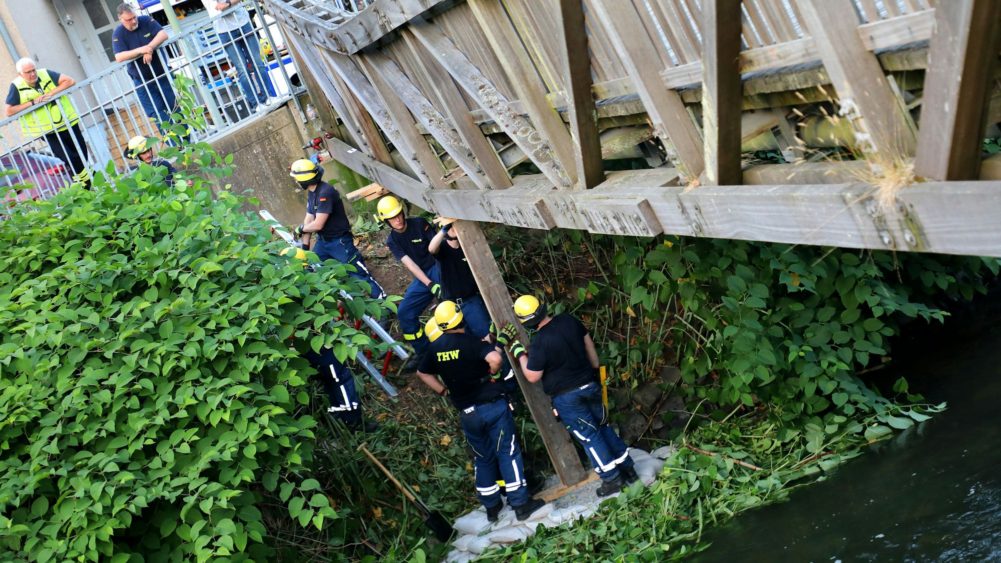 THW-Helfer stützen eine einsturzgefährdete Brücke mit einem Holzbalken ab.