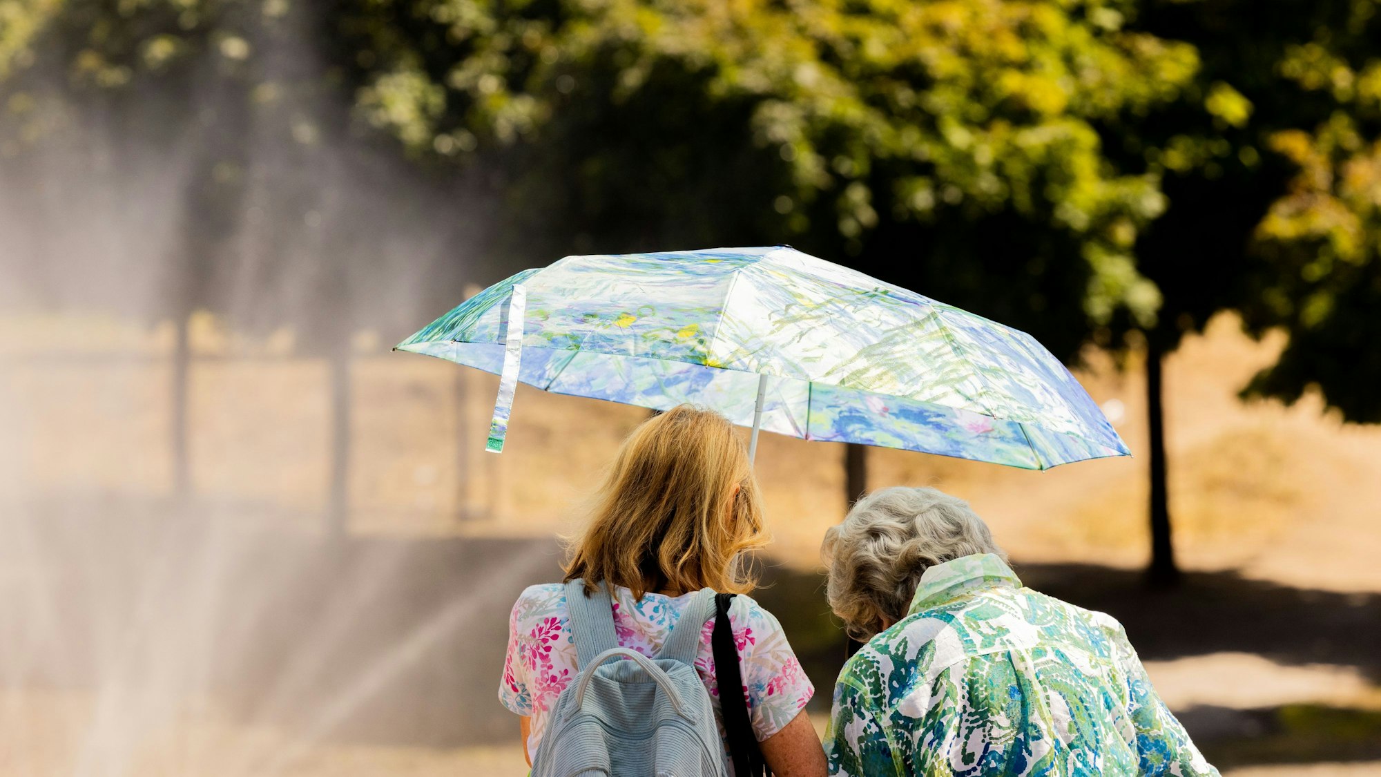 Zwei Frauen schützen am Rheinufer in der Altstadt mit einem Regenschirm vor der Sonne. +++ dpa-Bildfunk +++