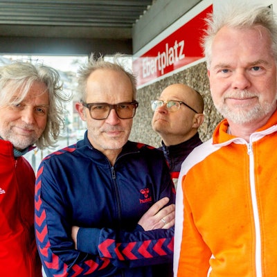 Die vier Mitglieder der Band Erdmöbel stehen in Trainingsanzügen an der Kölner Haltestelle Ebertplatz.