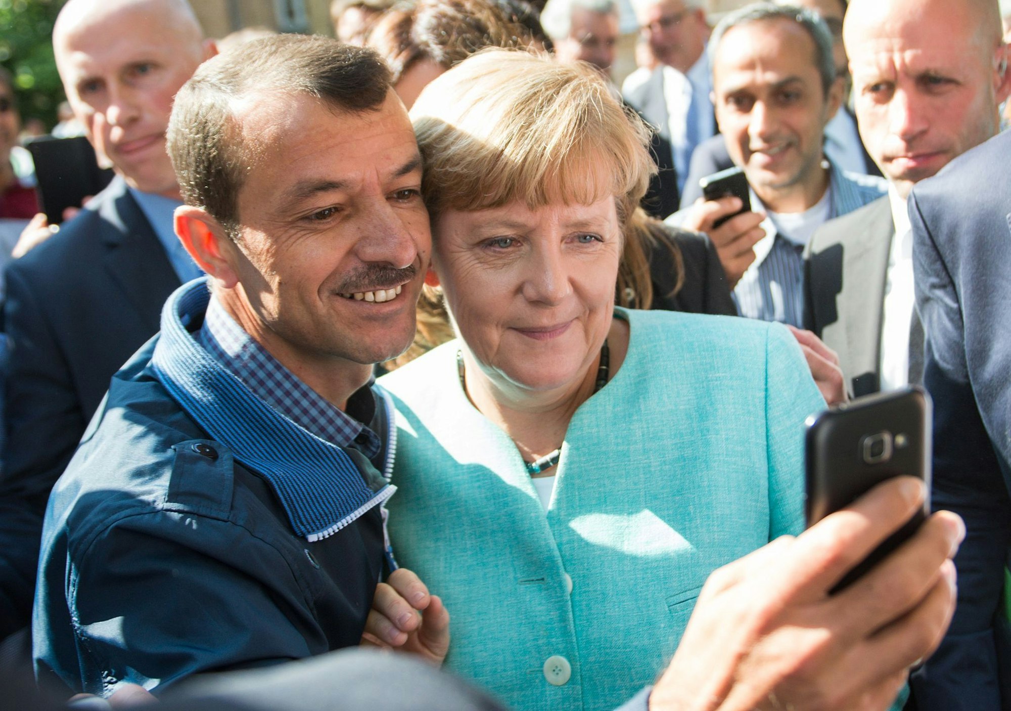 Bald zehn Jahre her: Angela Merkel (CDU) lässt sich nach dem Besuch einer Erstaufnahmeeinrichtung für Asylbewerber in Berlin-Spandau für ein Selfie zusammen mit einem Flüchtling fotografieren. (Archivbild)