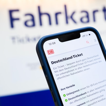 Eine Person hält am Hauptbahnhof ein Smartphone in der Hand, auf dessen Display eine Information zum Kauf des Deutschlandtickets zu sehen ist.