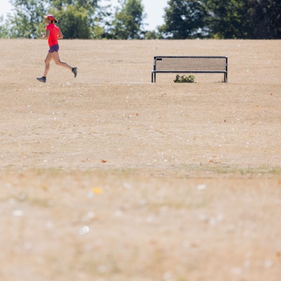 Eine Joggerin läuft in der Mittagshitze am Aachener Weiher durch vertrocknete Wiesen.