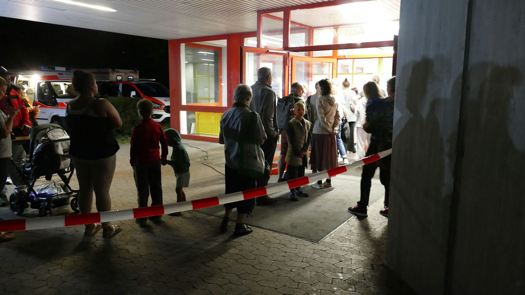 Vor der Turnhalle am Schulzentrum Neuenhof stehen Menschen Schlange, um sich registrieren zu lassen.