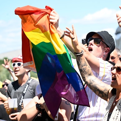 Konzertpublikum mit einer Regenbogenflagge im Sonnenschein.