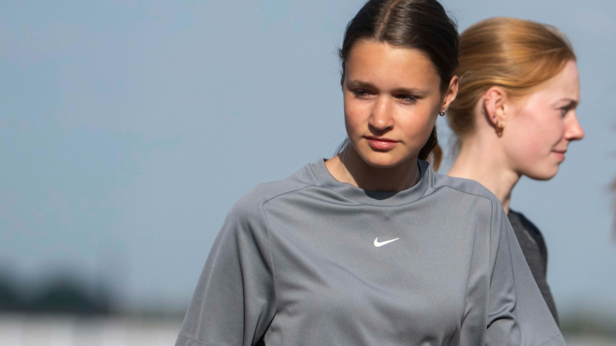 Zwei junge Sportlerinnen stehen hintereinander. Die vordere schaut nach links unten, die anderen nach rechts.