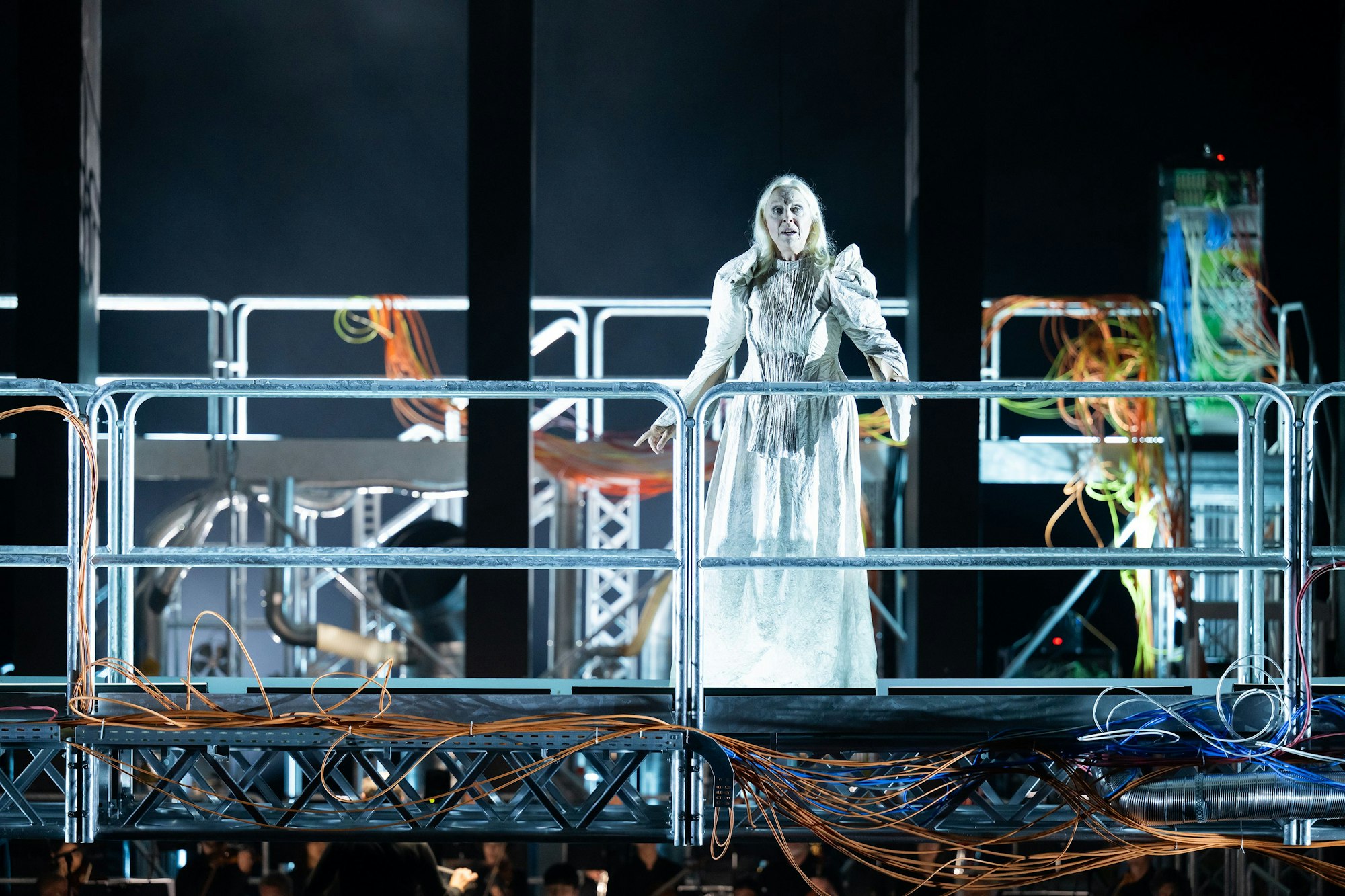 Anne Sofie von Otter singt im langen weißen Kleid auf dem Gestänge des Bühnenbilds.