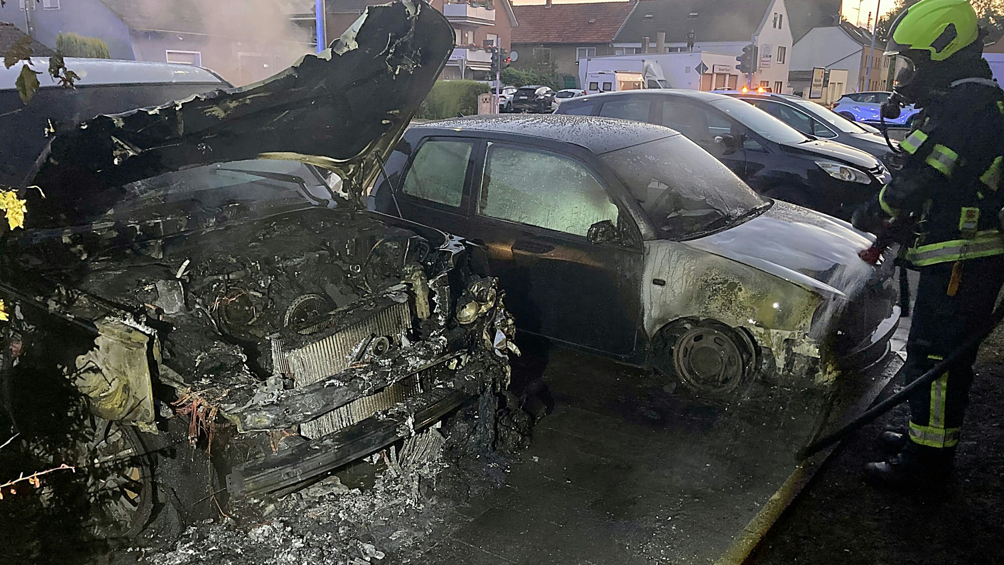 Auf dem Bild sind zwei ausgebrannte Autos und ein Feuerwehrmann zu sehen.