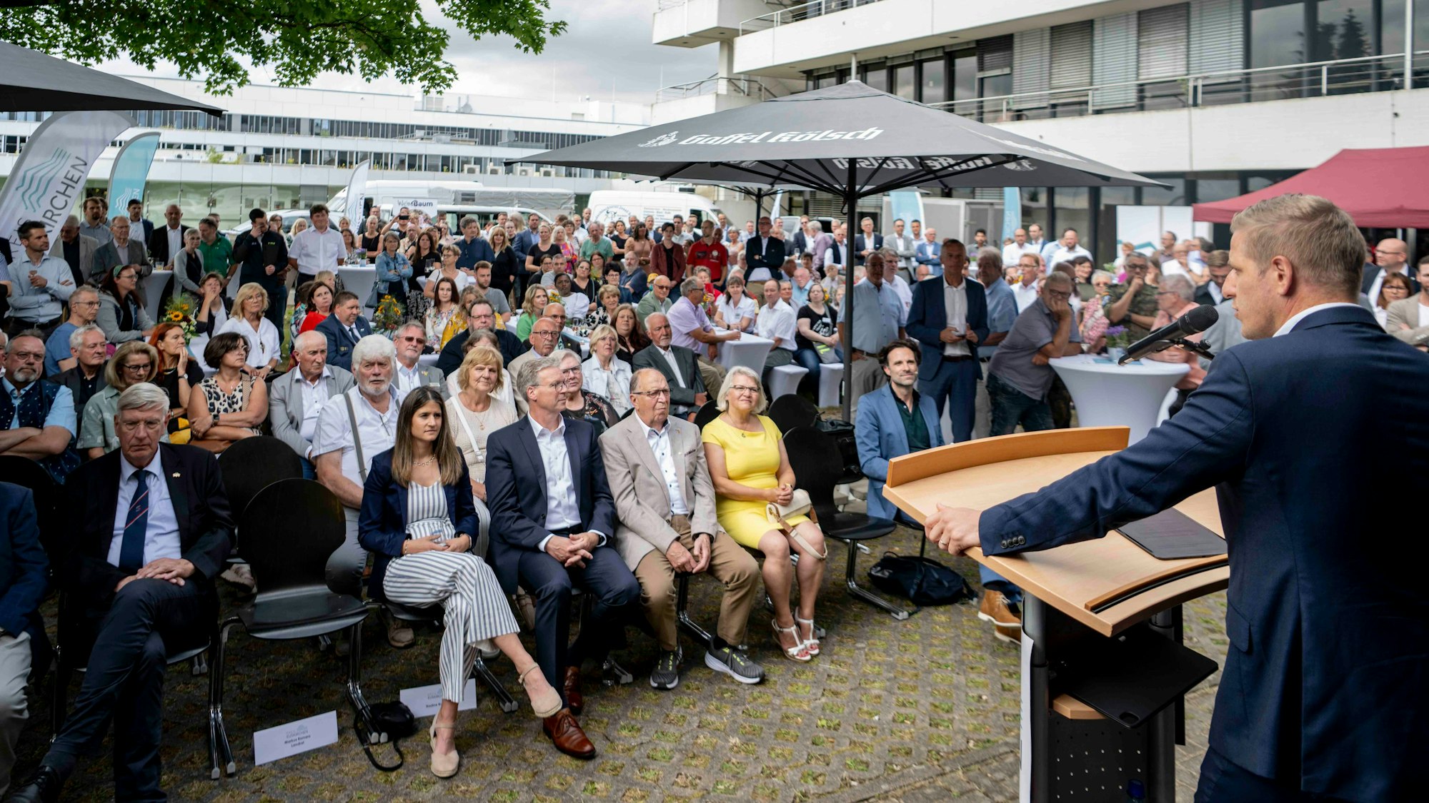 Markus Ramers, Landrat im Kreis Euskirchen, steht an einem Pult und spricht in ein Mikrofon. Vor ihm sitzen zahlreiche Menschen und hören zu.