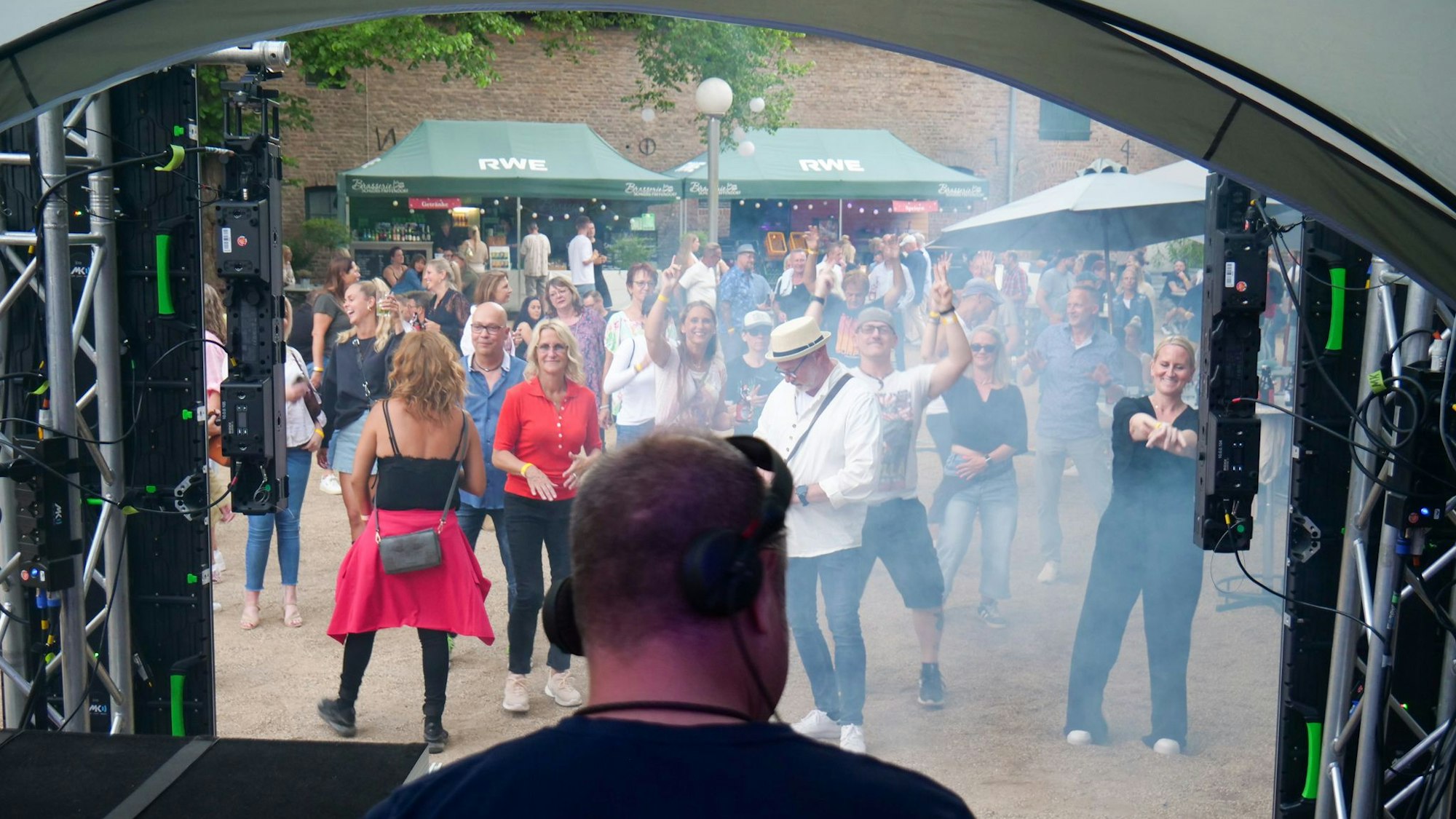 Ein DJ steht hinter seinem Mischpult, im Vordergrund tanzen Menschen.