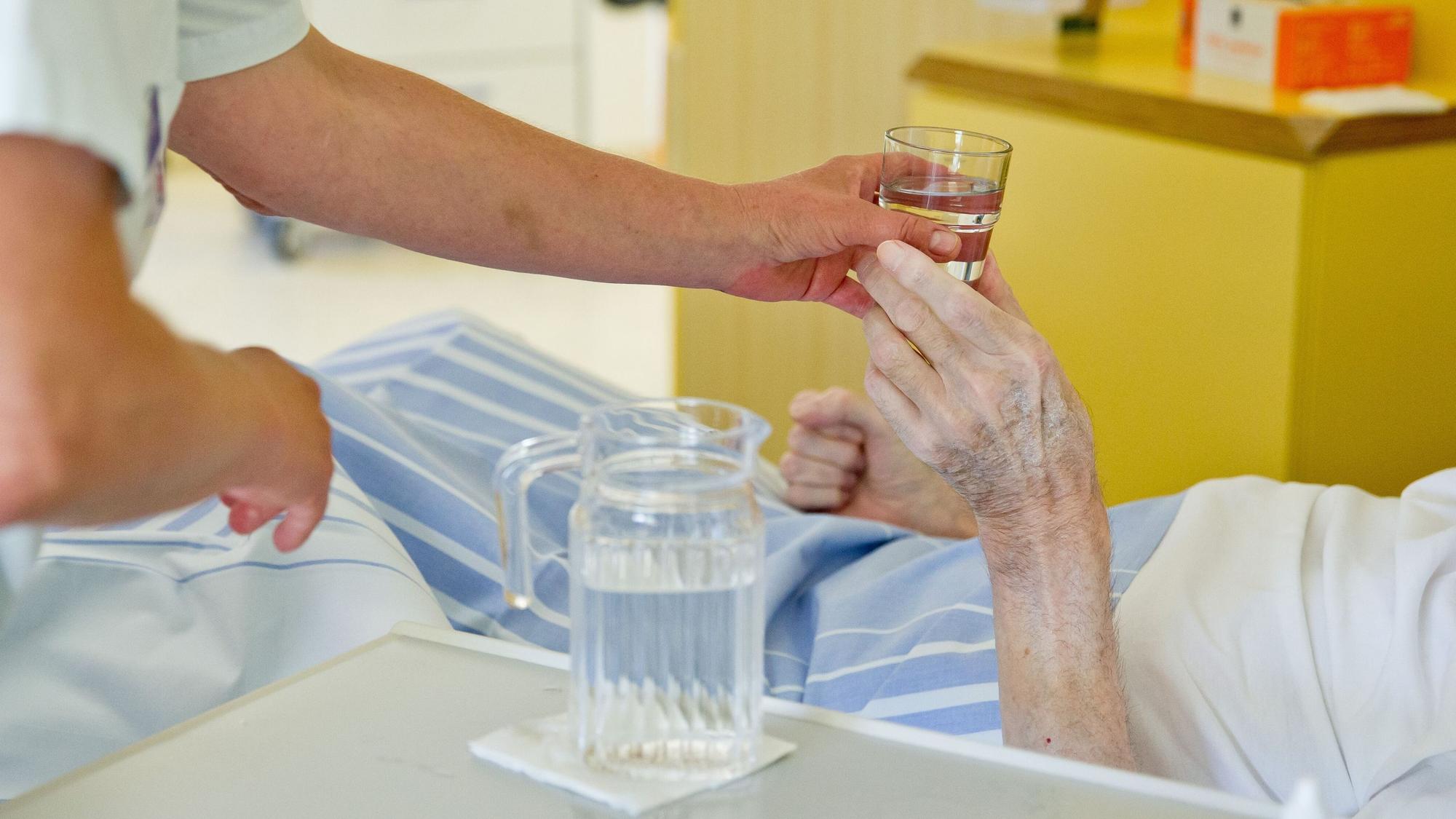 Eine Krankenpflegerin reicht einem Patienten ein Glas Wasser.