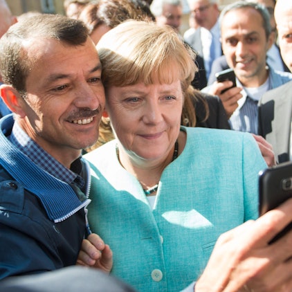 ARCHIV - 10.09.2015, Berlin: Bundeskanzlerin Angela Merkel (CDU) lässt sich nach dem Besuch einer Erstaufnahmeeinrichtung für Asylbewerber der Arbeiterwohlfahrt (AWO) und der Außenstelle des Bundesamtes für Migration und Flüchtlinge in Berlin-Spandau für ein Selfie zusammen mit einem Flüchtling fotografieren. (zu dpa: «Merkel mit Geflüchteten am Tisch - zehn Jahre nach 2015») Foto: Bernd von Jutrczenka/dpa +++ dpa-Bildfunk +++