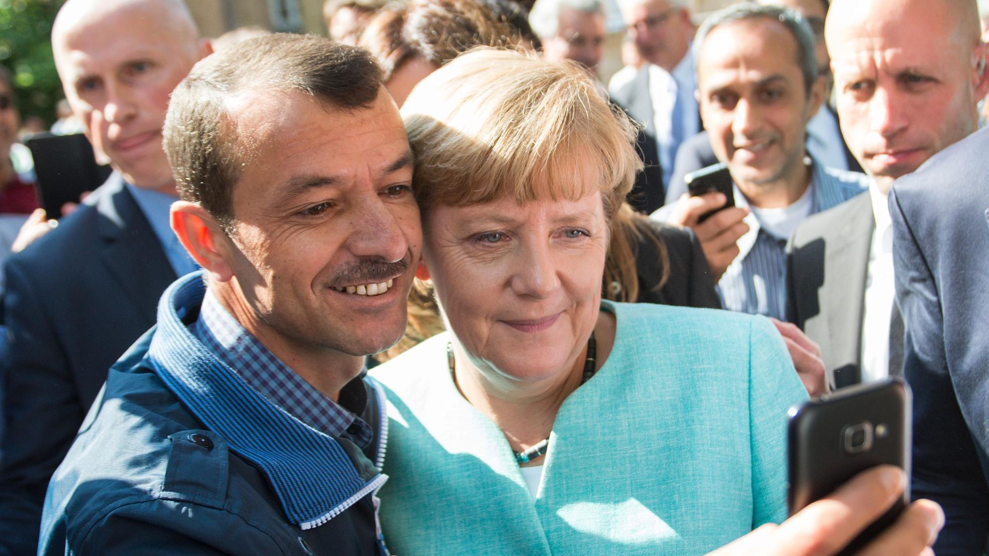 ARCHIV - 10.09.2015, Berlin: Bundeskanzlerin Angela Merkel (CDU) lässt sich nach dem Besuch einer Erstaufnahmeeinrichtung für Asylbewerber der Arbeiterwohlfahrt (AWO) und der Außenstelle des Bundesamtes für Migration und Flüchtlinge in Berlin-Spandau für ein Selfie zusammen mit einem Flüchtling fotografieren. (zu dpa: «Merkel mit Geflüchteten am Tisch - zehn Jahre nach 2015») Foto: Bernd von Jutrczenka/dpa +++ dpa-Bildfunk +++