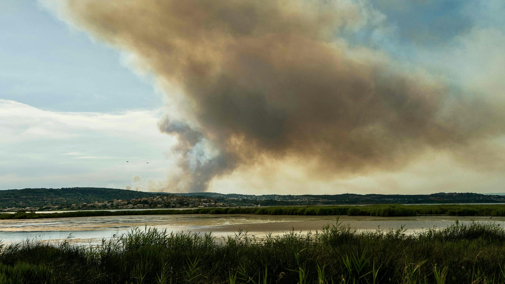 29.06.2025, Frankreich, Bizanet: Dieses Foto zeigt zwei Löschflugzeuge, die westlich der Stadt Narbonne im Südwesten Frankreichs, in der Nähe einer Rauchfahne, verursacht durch einen Waldbrand, an einem Berghang fliegen. Ein Teil des Corbières-Gebirges steht in Flammen, so dass die Abtei Fontfroide und ein Campingplatz vorsorglich evakuiert werden mussten, wie die Präfektur und die Feuerwehr des Departements mitteilten. Foto: Idriss Bigou-Gilles/AFP/dpa +++ dpa-Bildfunk +++